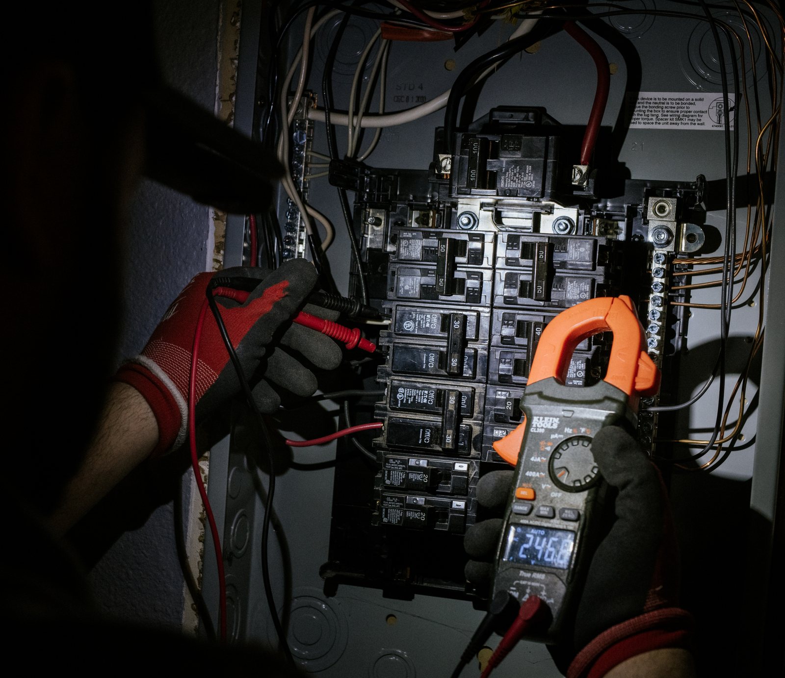 Tioga Plumbing electrician testing a breaker panel with a clamp meter in a DFW home