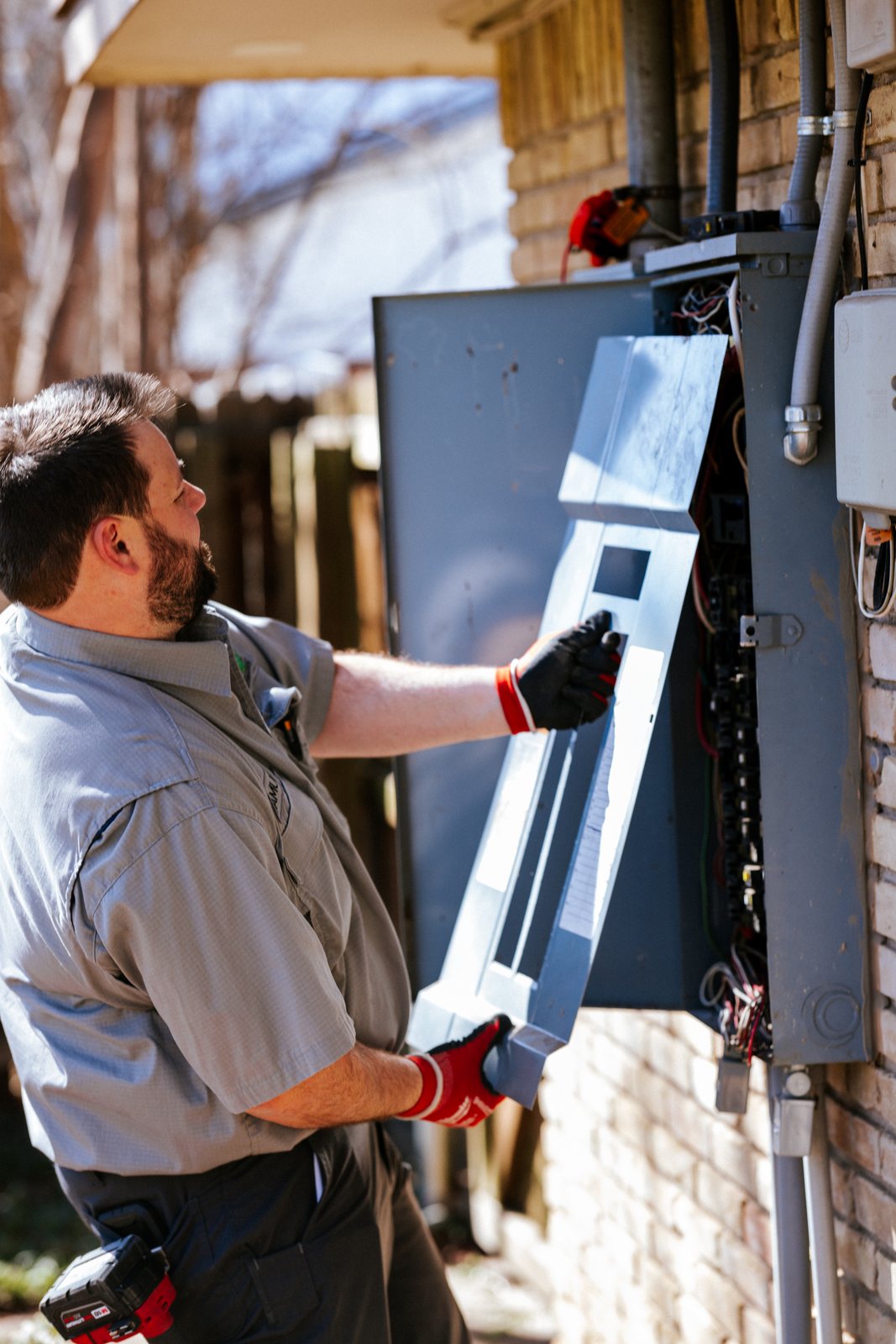 Tioga Plumbing technician opening an exterior electrical panel at a DFW home