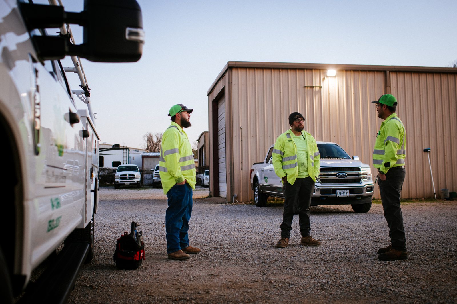 Three Tioga Plumbing technicians talking by a service truck in the Hurst, TX yard at sunrise