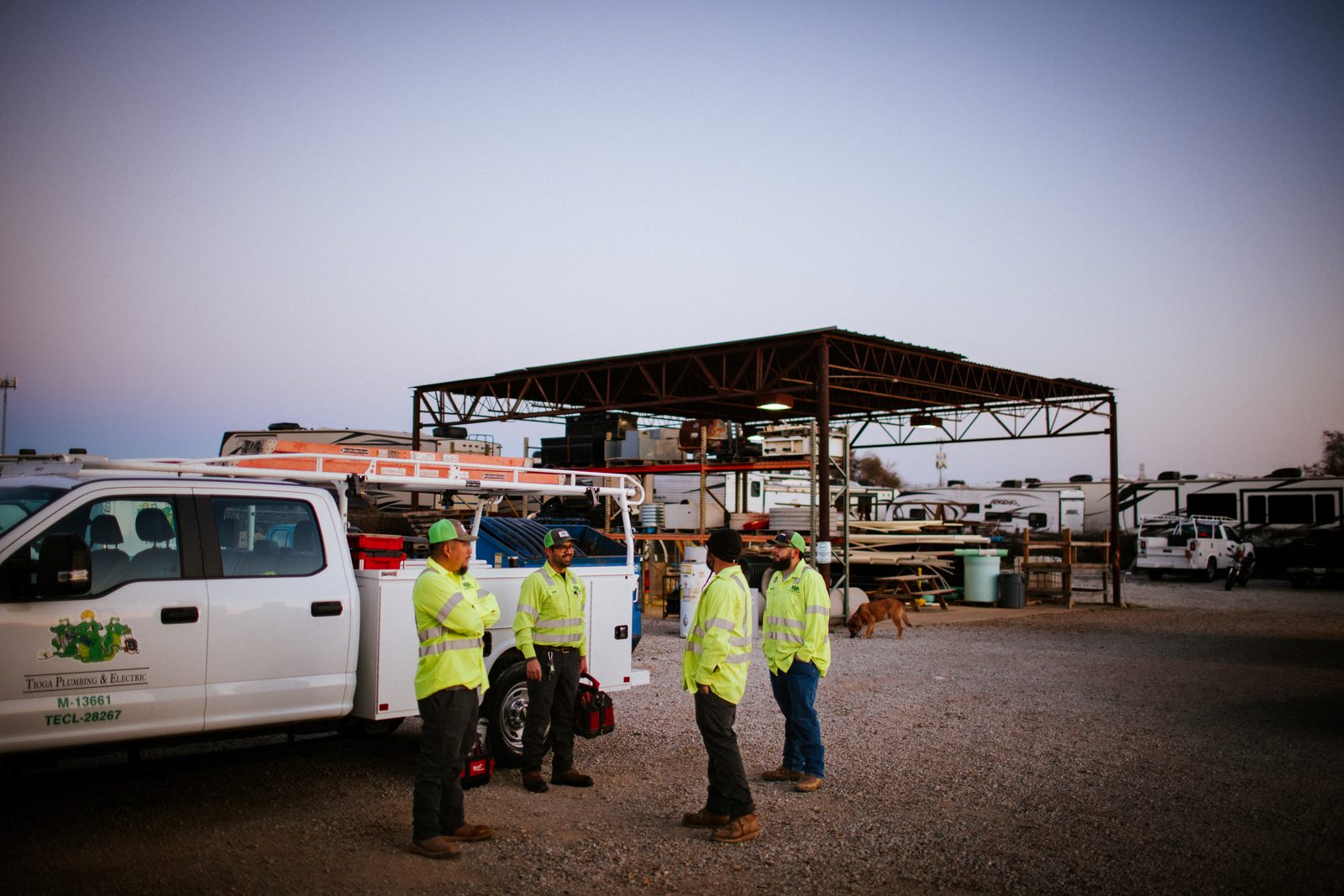 Tioga Plumbing service trucks and crew under the yard canopy in Hurst, TX at dawn