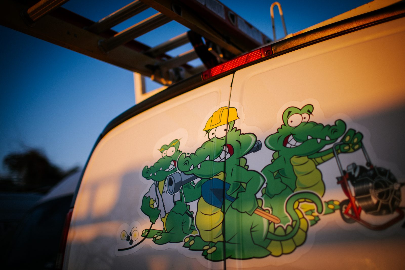 Ladder-racked Tioga Plumbing van with the gator crew decal at sunset