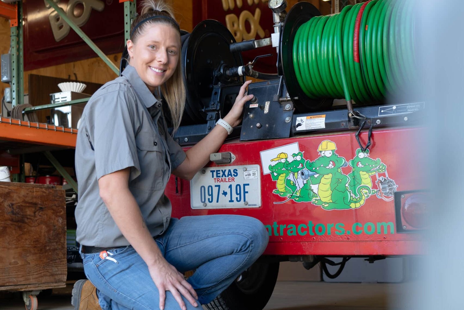 Tioga Plumbing technician kneeling beside the hose reel on the company's hydro-jetting trailer at the Hurst, TX shop
