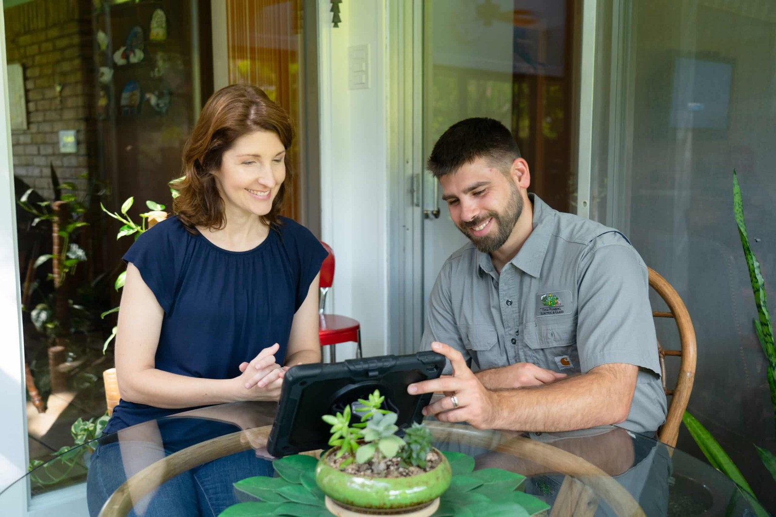 Tioga Plumbing technician sitting with a DFW homeowner at her kitchen table, going over a repair estimate on a tablet