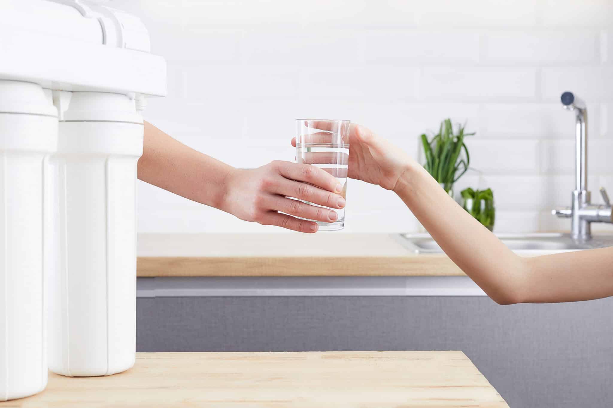 A water filtration system beside a female hand offering a glass of clean water, symbolizing purified water and a healthy life concept.