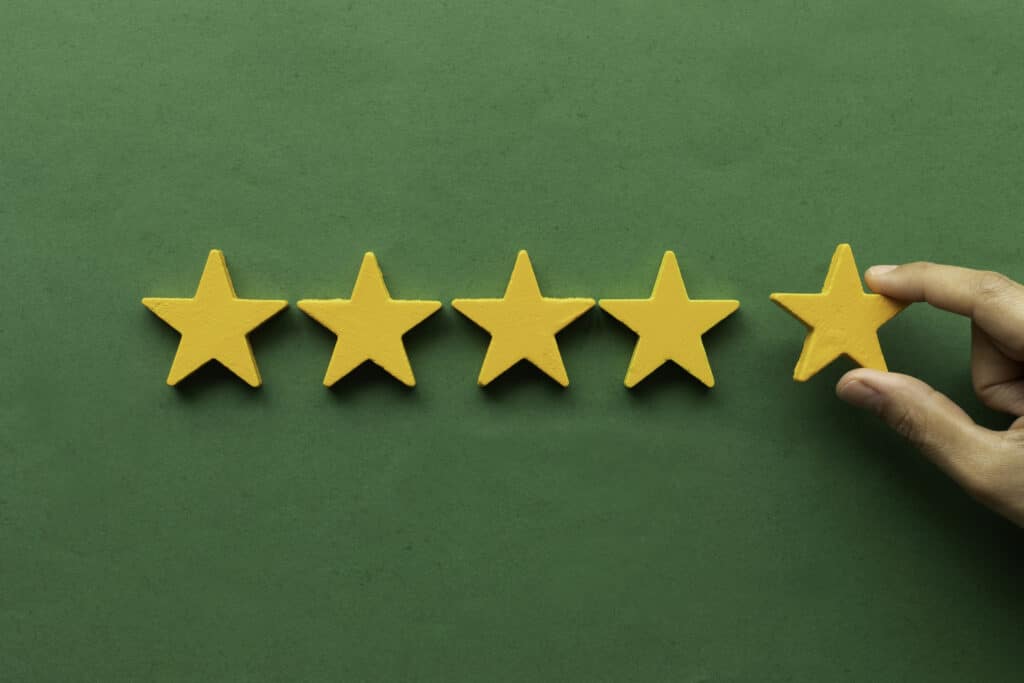 Five-star rating feedback. A hand is holding the last star shape in front of a green-colored background, giving the highest score to the review of the Sump Pump service by Tioga Plumbing & Electric